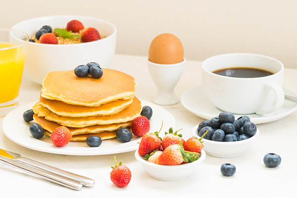 Conjunto de pequeno-almoço saudável com Panqueca e Granola com mirtilo e morango e café preto , Leite e sumo de Laranja 