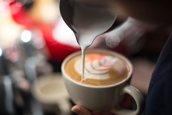 Mão de barista a fazer café com leite ou cappuccino a verter leite a fazer latte art