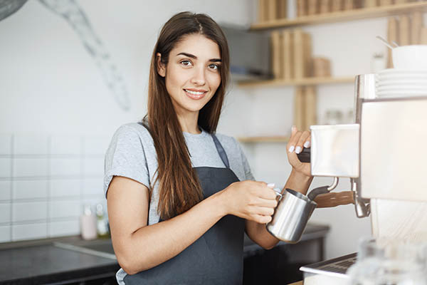 Senhora barista experiente leite desnatado num jarro a olhar para a câmara a sorrir