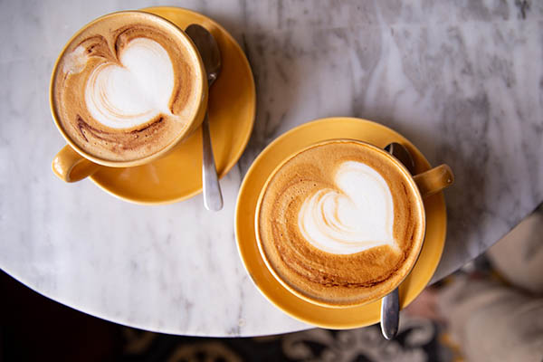 Duas chávenas amarelas de cappuccino quente com forma de coração como latte de arte.